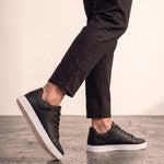 Men's Black Faux Leather Minimalist Low-Top Trainers, the shoes in mid-step, showing the sole.