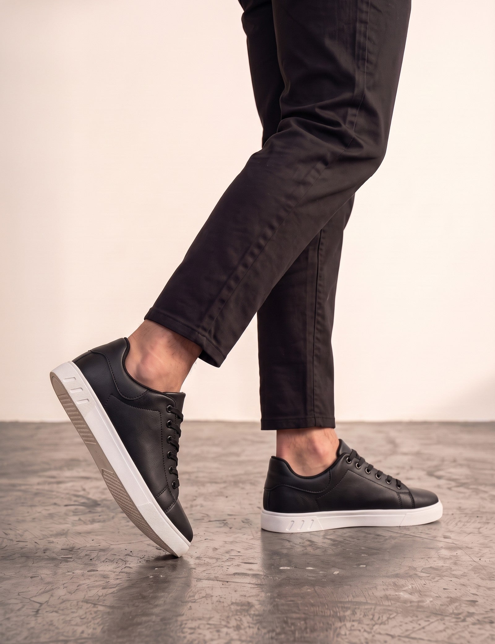 Men's Black Faux Leather Minimalist Low-Top Trainers, the shoes in mid-step, showing the sole.
