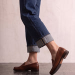 Men's Brown Penny Loafers with Moccasin Stitching, the shoes in mid-step, showing the sole.