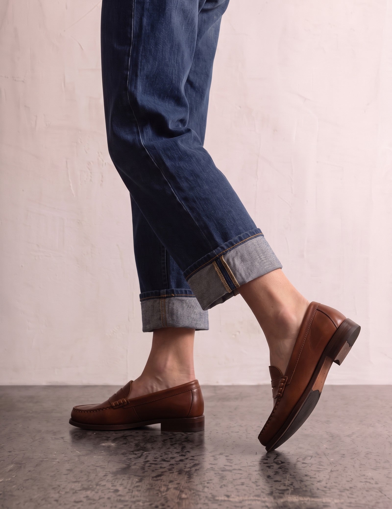 Men's Brown Penny Loafers with Moccasin Stitching, the shoes in mid-step, showing the sole.