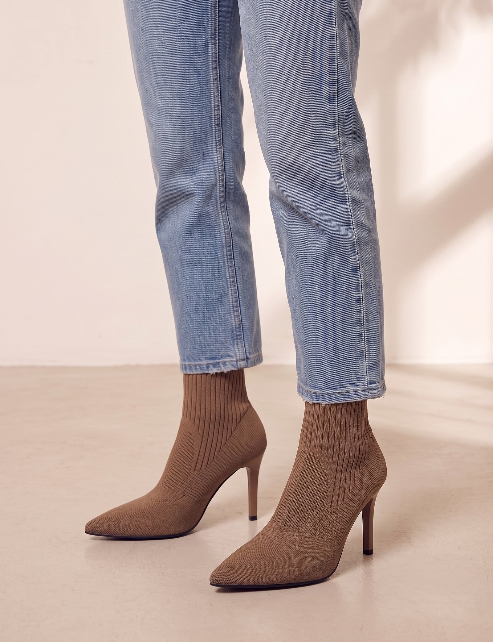 Women's Taupe Ribbed Knit Stiletto Sock Boots, three-quarter front view of the shoes, worn.