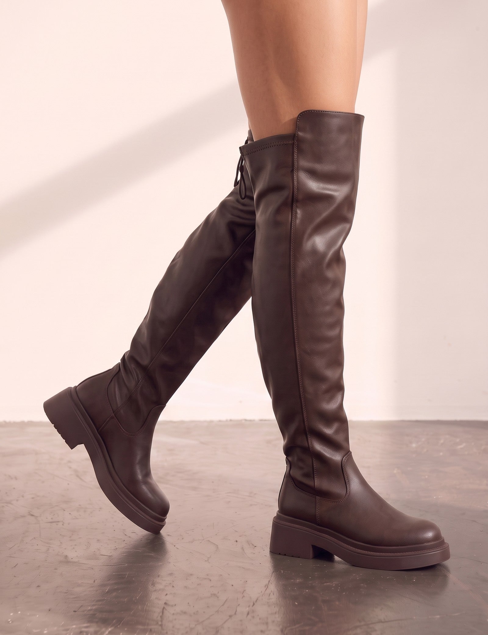 Women's Brown Leather-Look Platform Over-the-Knee Boots, the shoes in mid-step, showing the sole.