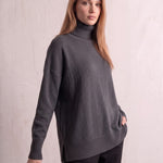 Women's Relaxed Fit Roll Neck Jumper in Dark Grey, three-quarter view from the left, full length.